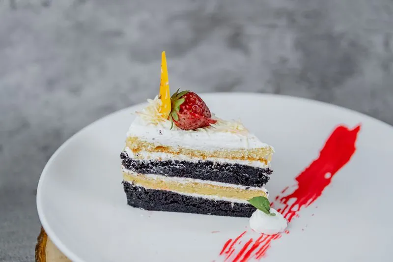 A slice of cream cake with a strawberry on a white plate
