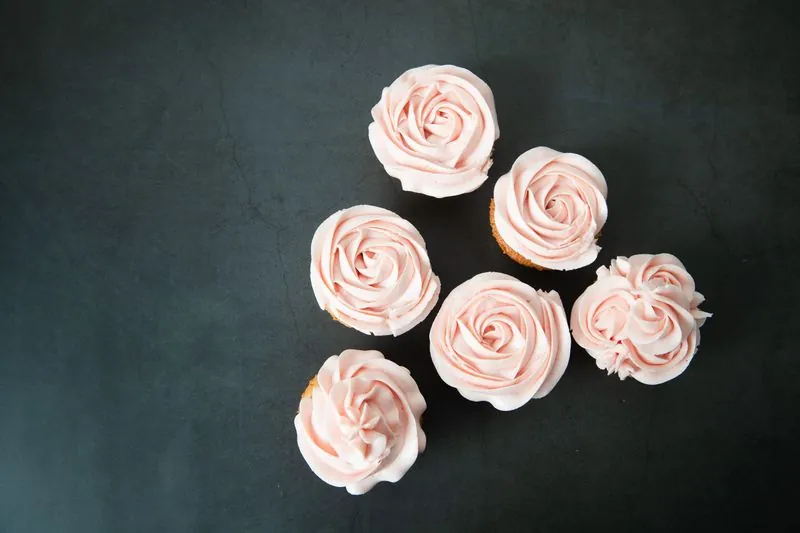Six cupcakes with pale pink frosting on a dark surface